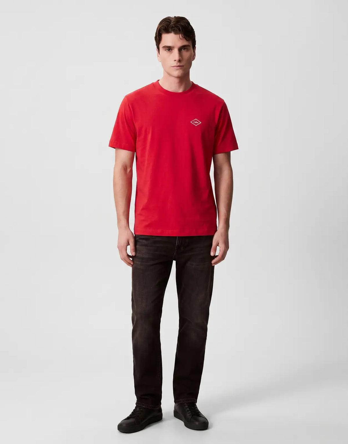 A male model wears a Calvin Klein 20s Matchbox Graphic Red T-Shirt, featuring a white diamond logo on the chest, paired with