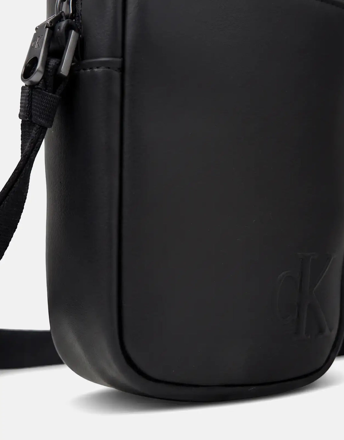 Black Calvin Klein Bold Slim Reporter Bag, close-up showing smooth material, embossed 'CK' logo, and a shoulder strap.