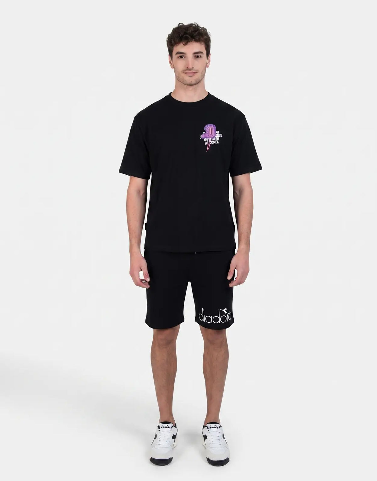 Diadora Vado Black T-Shirt featuring a purple and pink graphic, worn by a male model with black shorts and white sneakers.