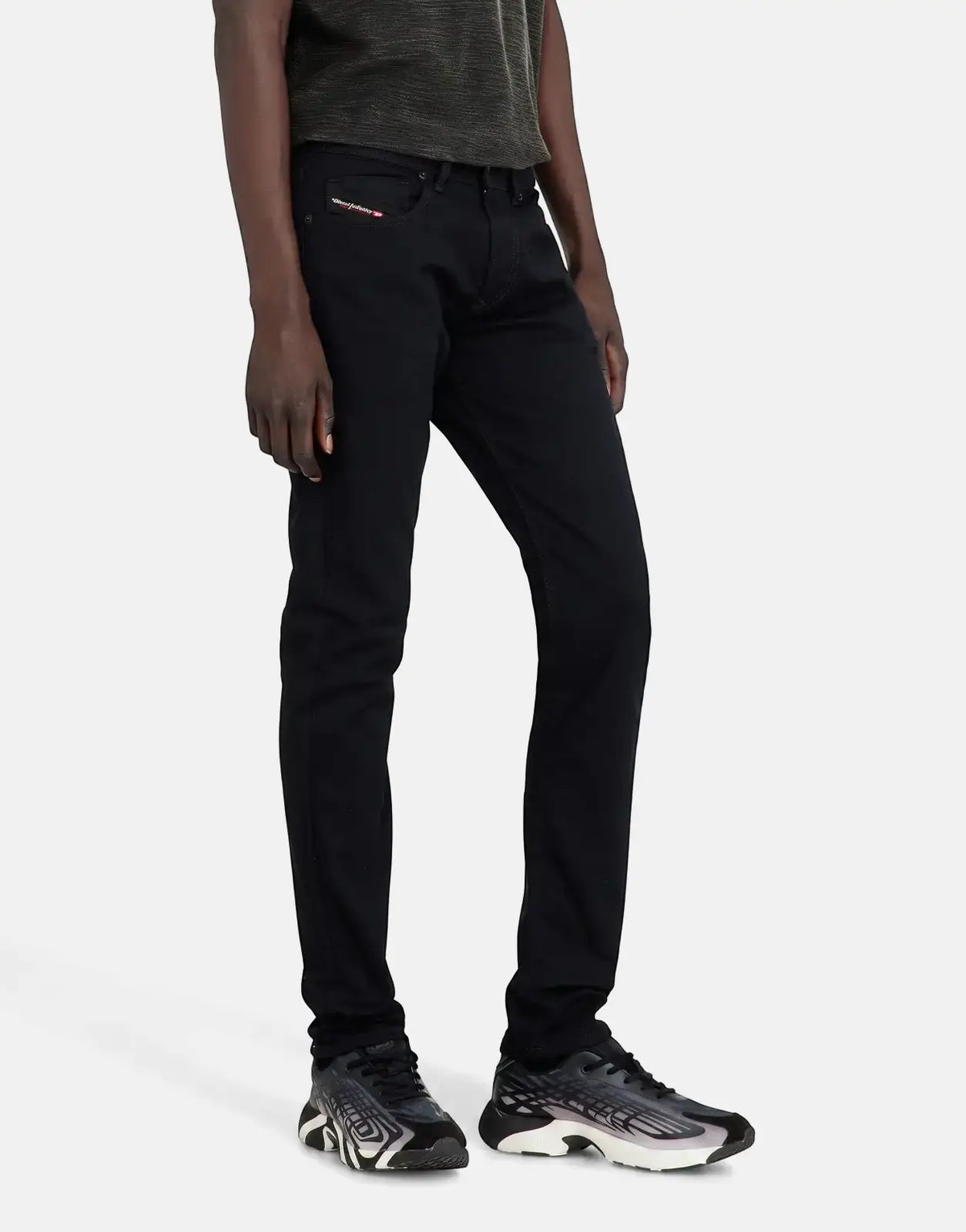 Full-length view of a person wearing black Diesel 1979 Sleenker skinny jeans and patterned sneakers, modeled on a white