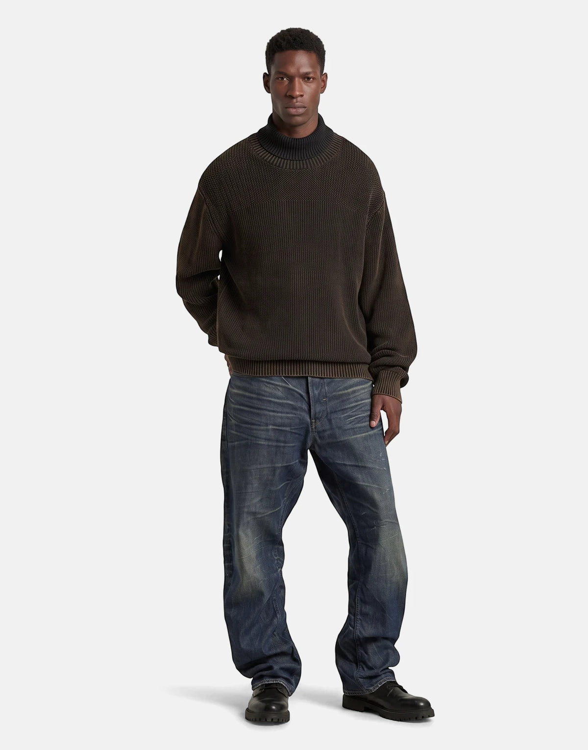 Male model wearing G-Star RAW Arc 3D Loose Raw Vintage Jeans in blue, paired with a dark brown chunky knit turtleneck