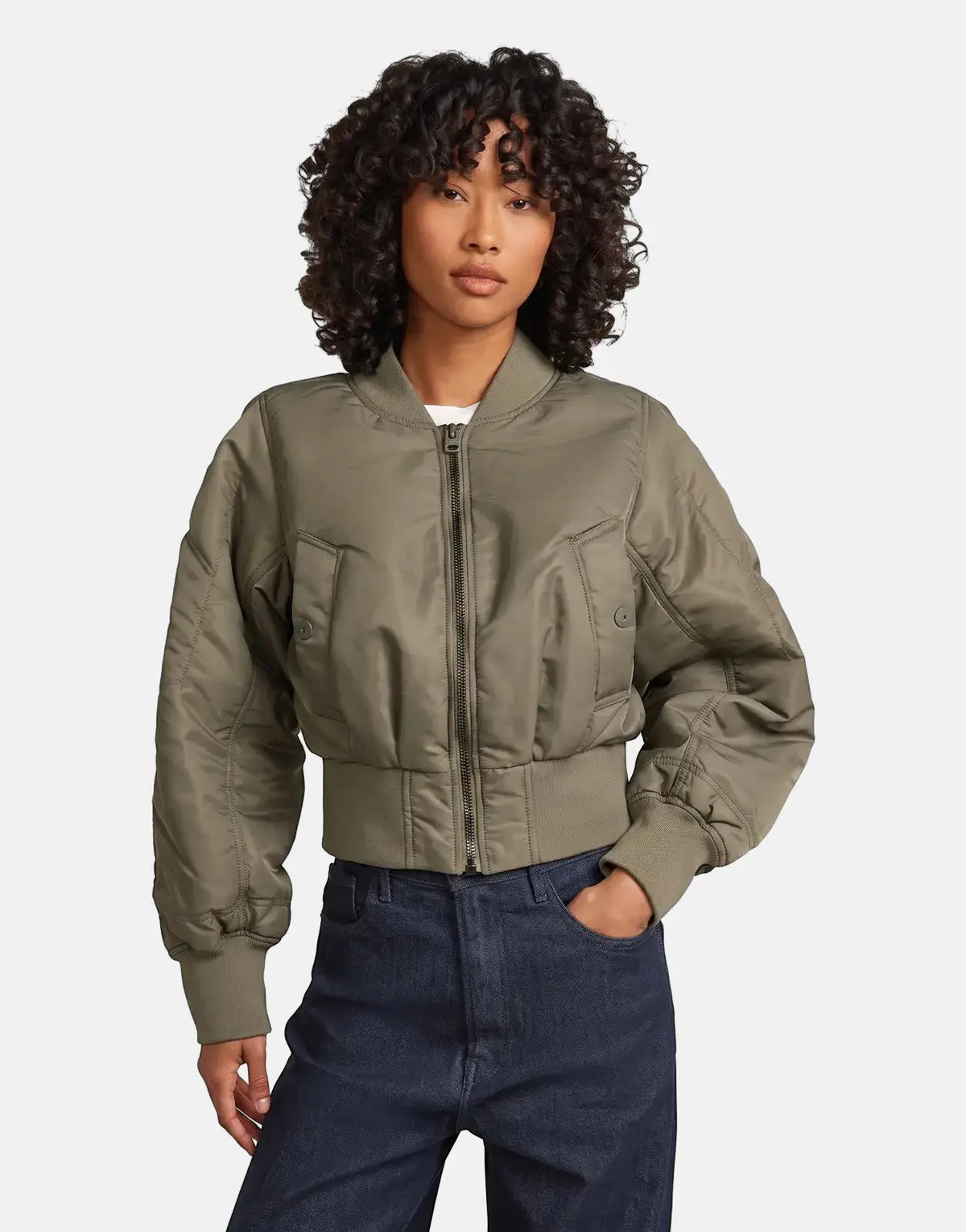 Woman wearing an olive green G-Star RAW Bomber Turf jacket, standing, with her right hand in her dark jeans pocket.