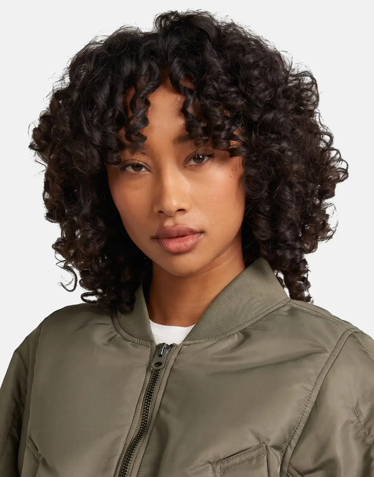Close-up of a woman with curly hair wearing an olive green G-Star RAW Bomber Turf jacket, facing forward.