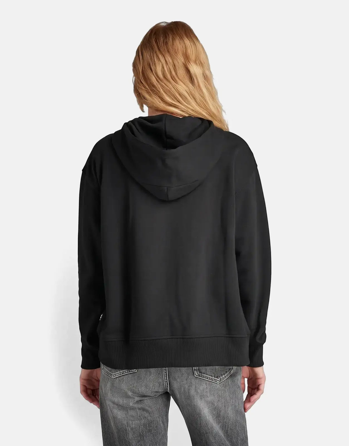 Woman wearing a G-Star RAW Graphic Core Hood in dark black, paired with dark wash jeans, shown from the back.