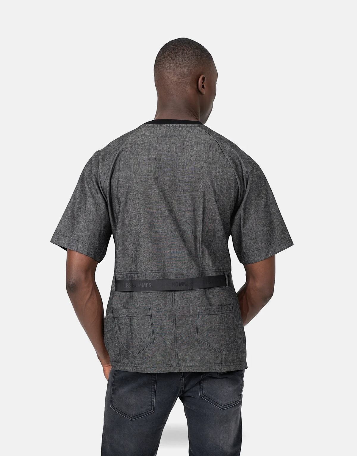 Back view of a man wearing a Les Hommes grey short-sleeved t-shirt with a black belt detail and dark grey jeans.
