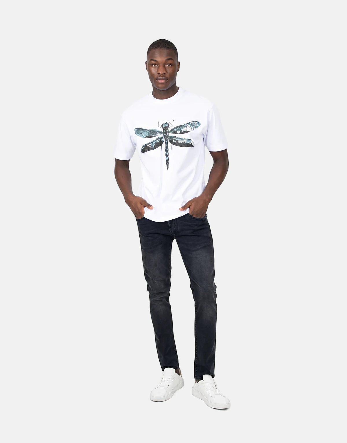 Black male model wearing a Les Hommes Dragonfly White T-Shirt paired with black distressed jeans and white sneakers.