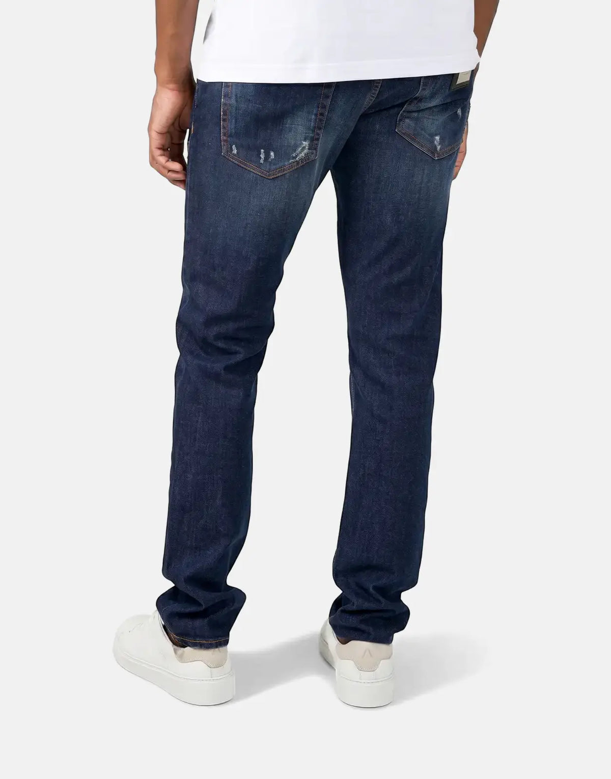 Men's Les Hommes dark wash jeans with distressed details and brown stitching, seen from the back paired with white sneakers.