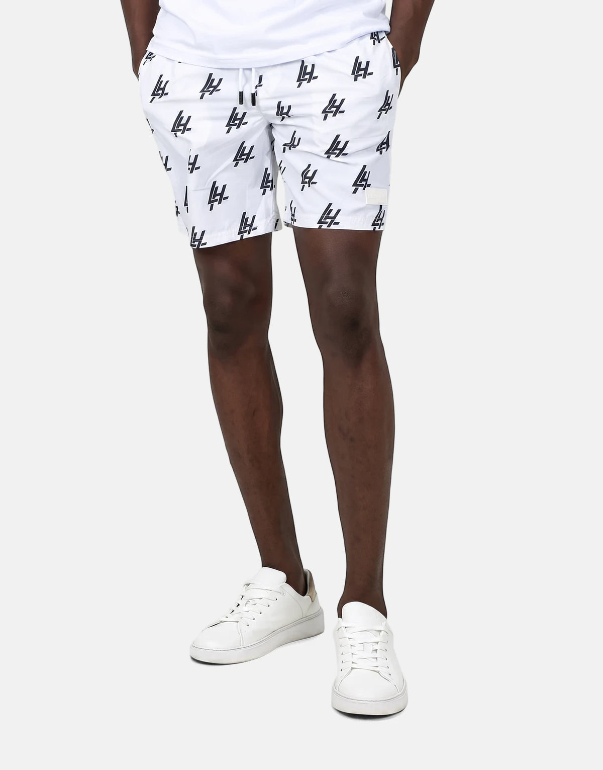 Les Hommes white swim shorts with black print on a standing model, showcasing the fit and details of the swimwear.