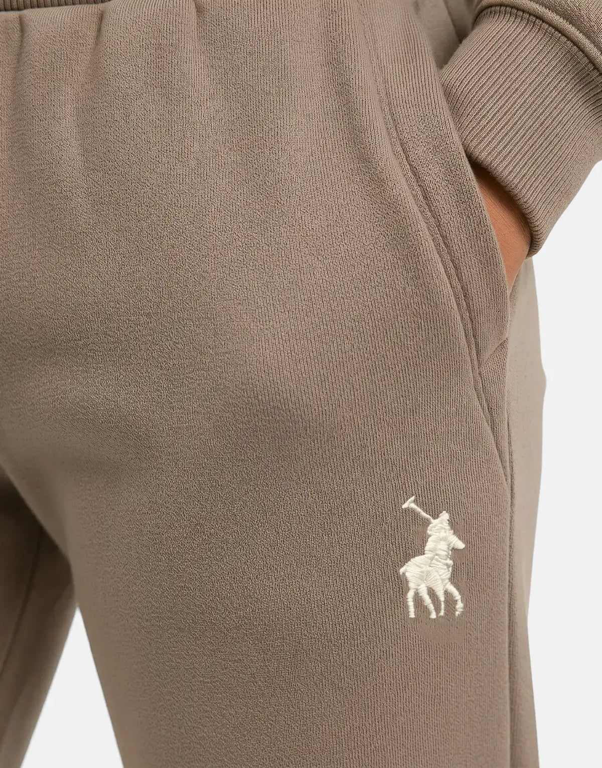 Close-up of brown Polo Girls Kim Pull On Iron Jogger, featuring an embroidered logo and a visible pocket with a hand inside.