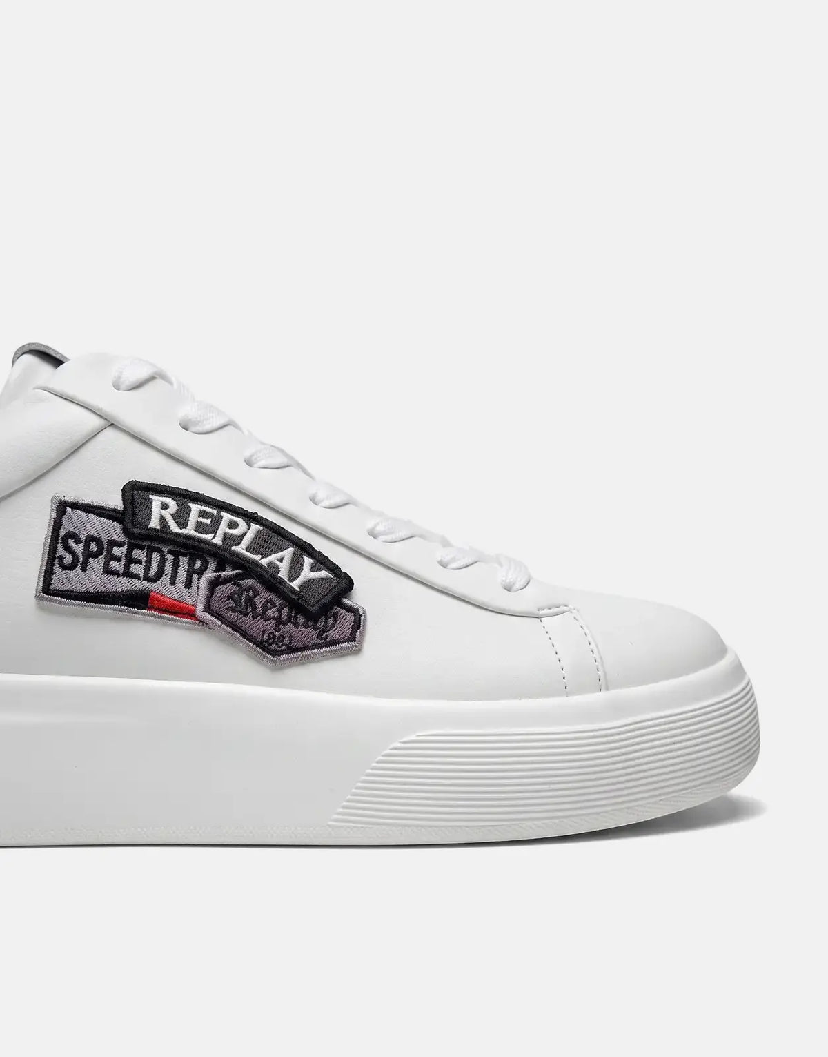 Close-up of a white Replay Notting Badges sneaker, featuring embroidered 'REPLAY' and 'SPEEDTRIP' patches, white laces, and