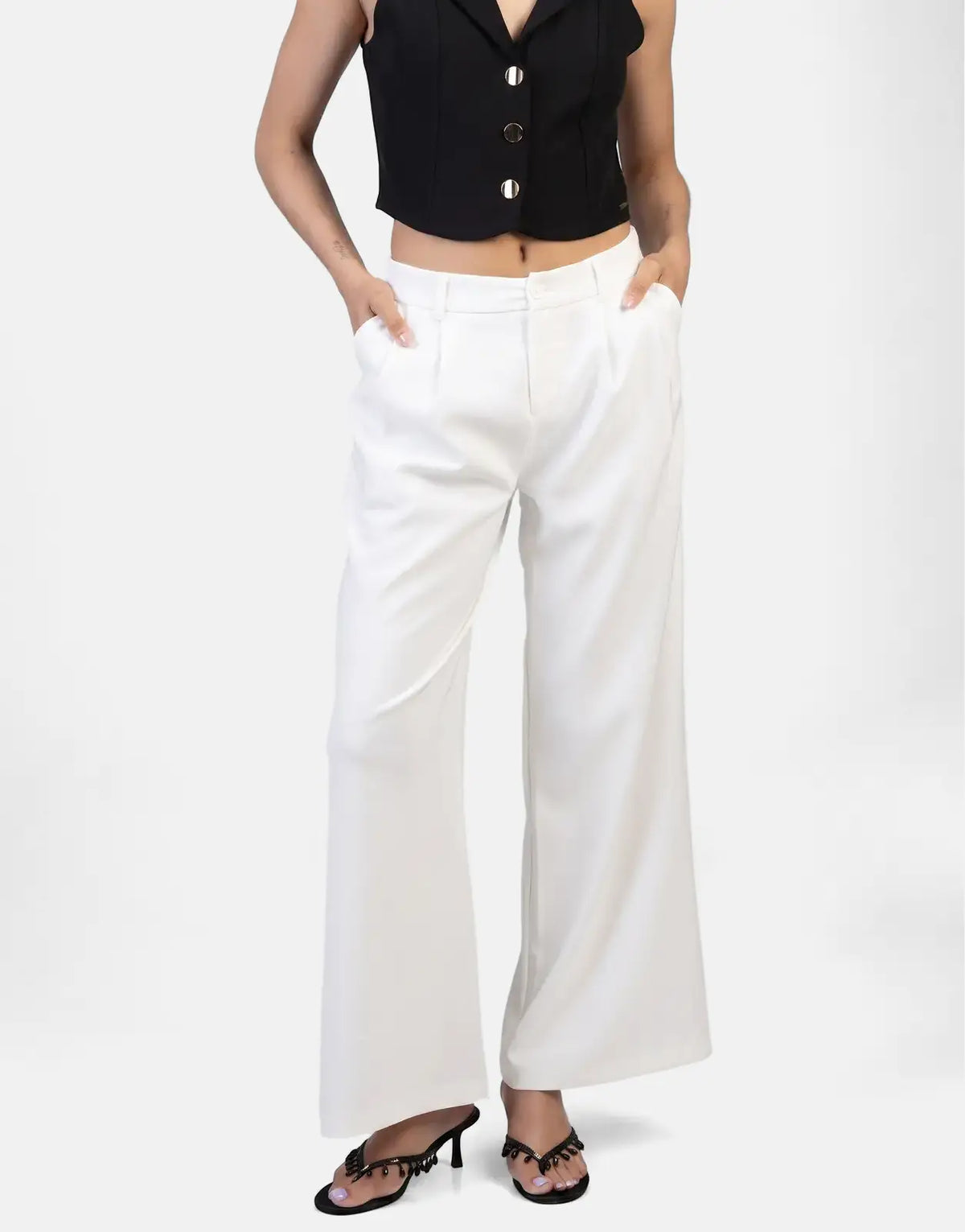 Model wearing Sissy Boy Alice wide leg off-white trousers, paired with a black sleeveless top and black embellished sandals.