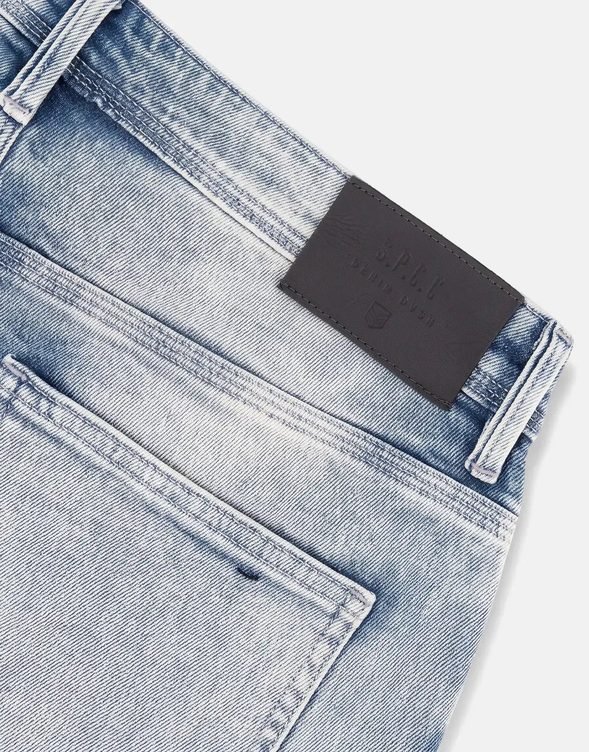 Close-up of SPCC Subzero Bleach Jeans, light blue washed denim with visible back pockets and a black leather brand patch on