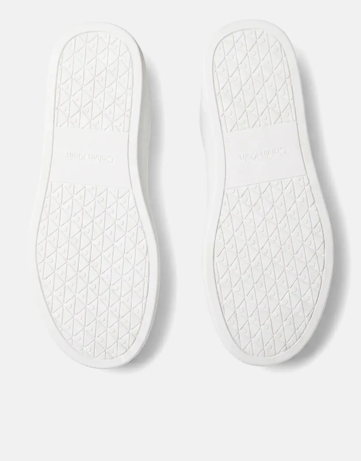 Bottom view of two white Calvin Klein Classic Cupsole sneakers, showcasing their patterned soles and brand logo.