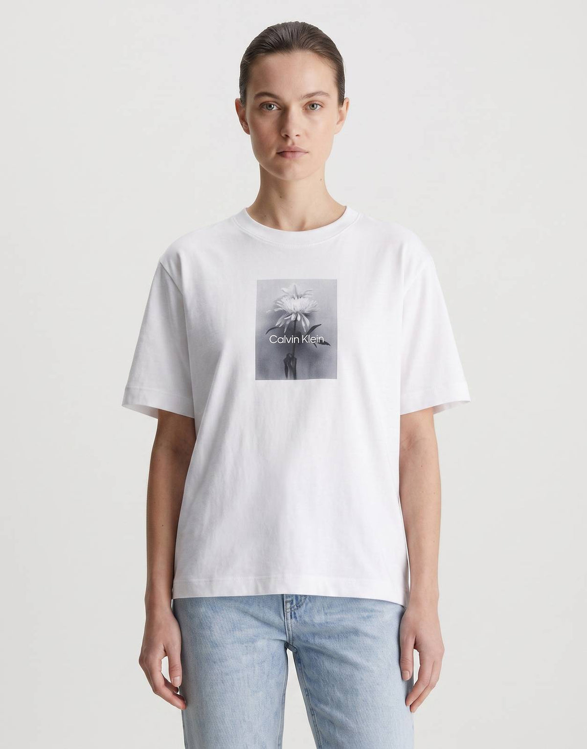 A woman wears a white Calvin Klein Flower Boxy T-Shirt with a black and white floral graphic print.
