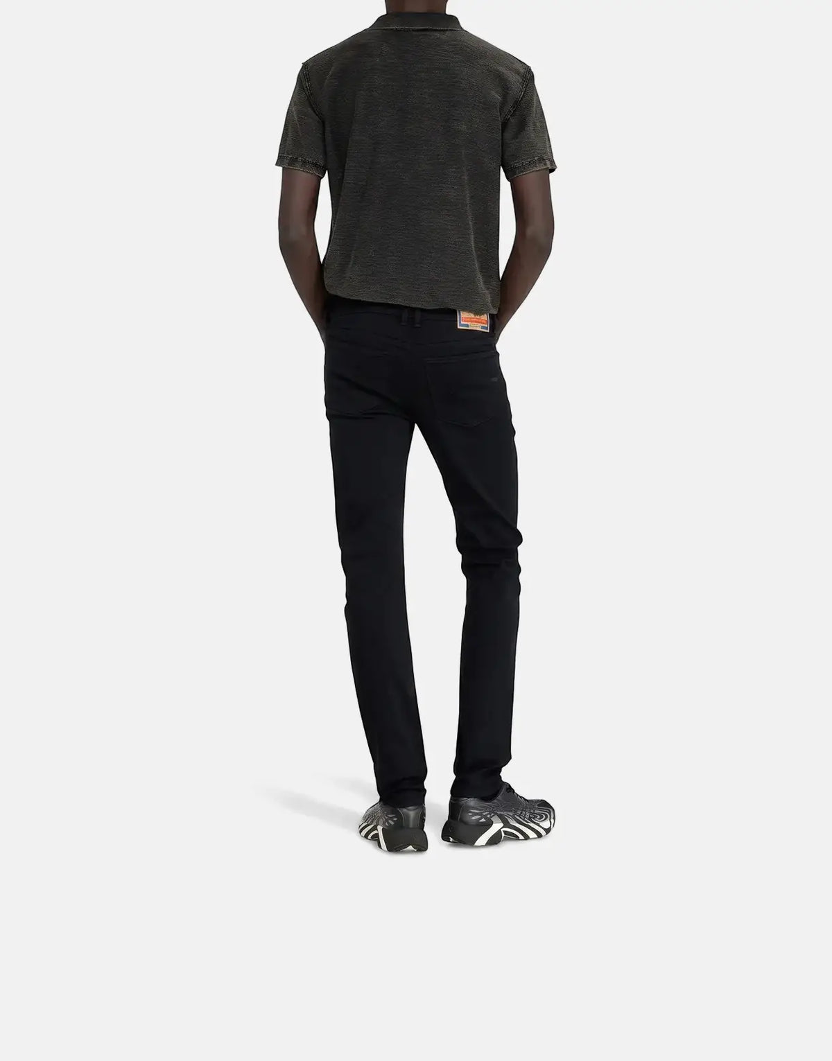Back view of a male model wearing Diesel 1979 Sleenker skinny jeans in black, paired with a dark polo shirt and sneakers.