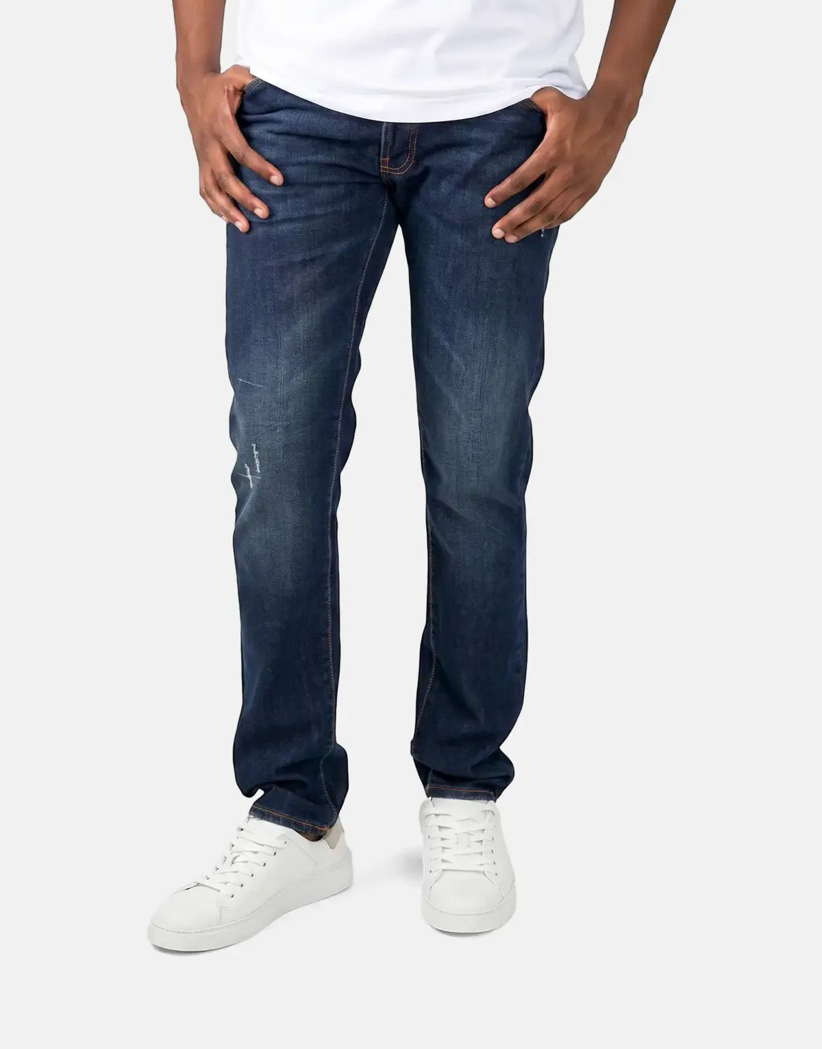 A person wears Les Hommes dark wash slim-fit jeans paired with white sneakers, hands casually in pockets.