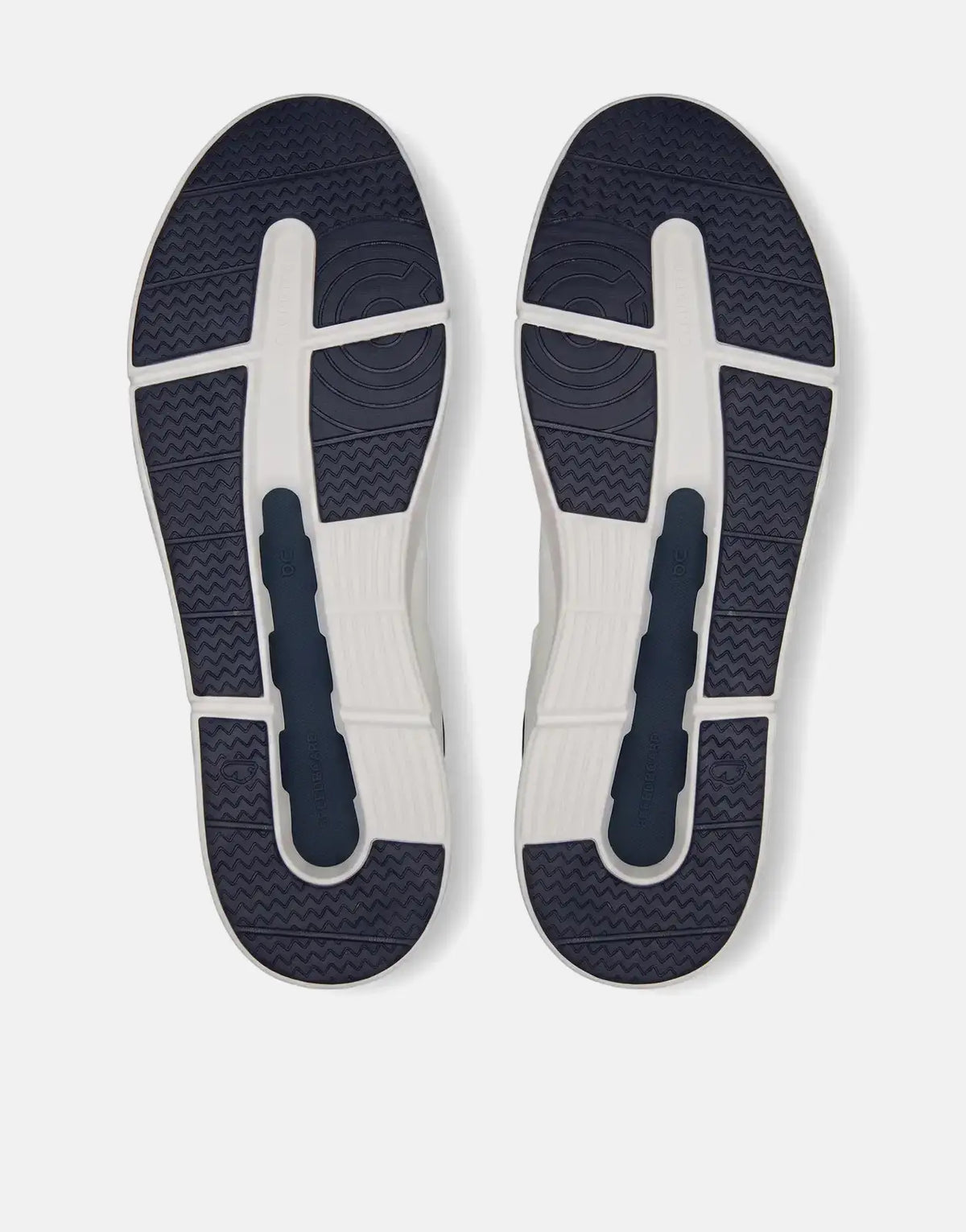 View of the soles of two white and navy blue On Men's The Roger Advantage sneakers with detailed tread.