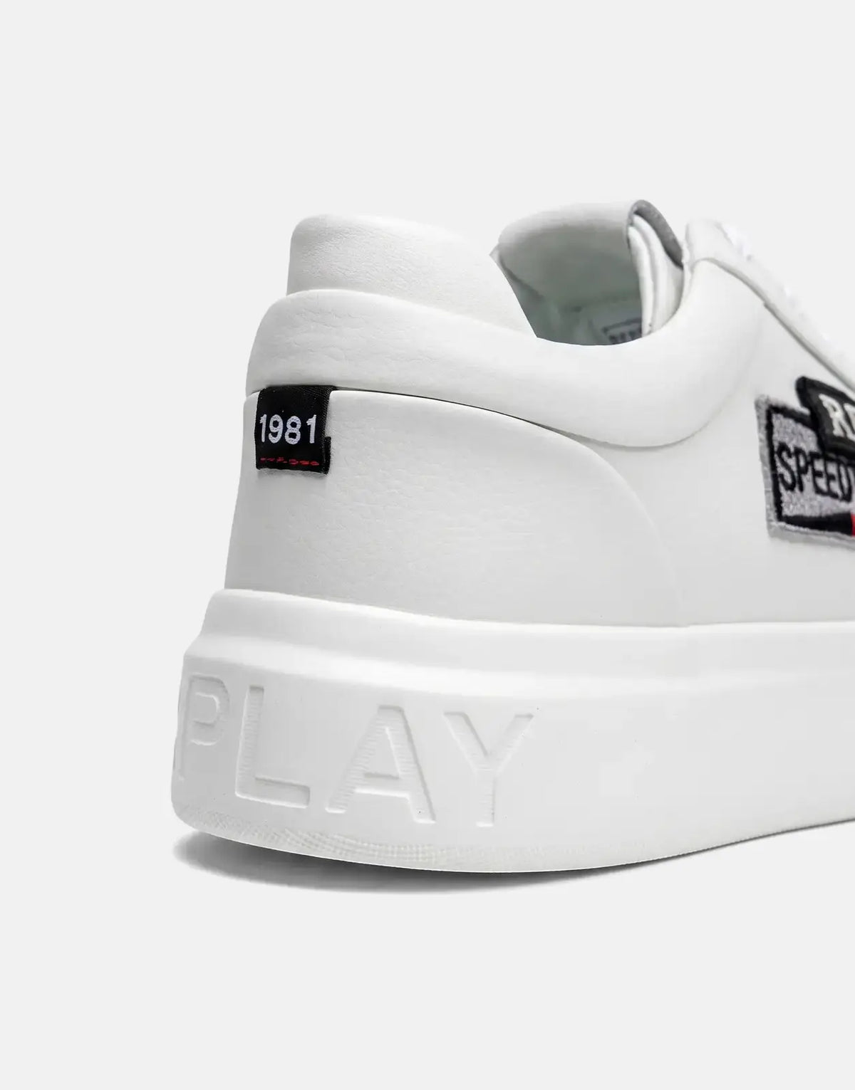 Close-up of the heel and side of a Replay Notting Badges white sneaker, featuring a '1981' tag and 'Replay Speedway' patch.